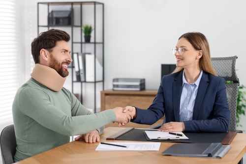 A man in a neck brace shaking hands with a motorcycle accident lawyer to agree on a settlement amount.
