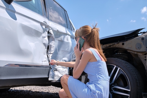 Woman calling her insurance company while looking at the damage on her car and will seek the help of a car accident lawyer.